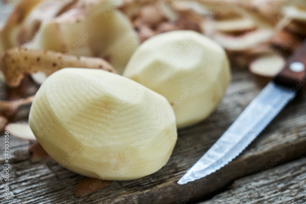 Peeled potatoes with a knife and potato peel on the rough wooden a country table Peeled potatoes with a knife and potato peel on the rough wooden a country table