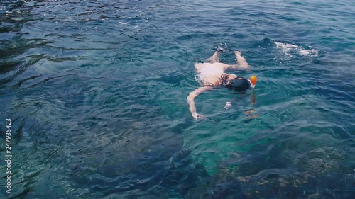 Young woman snorkeling and making underwater photo video with mobile phonee in the blue tropical water wearing white swimsuit. photo