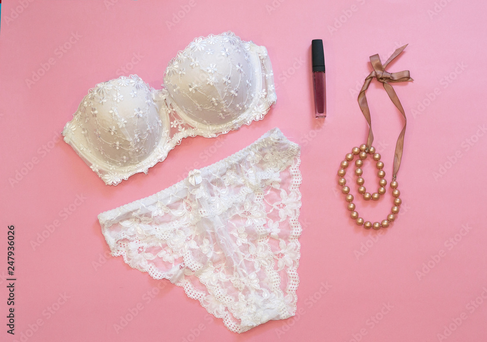 White lacery lingerie near lipstick and necklace on pink background. Woman  underwear for special occasions. Composition for beauty blog, magazine  article, flat lay, top view. Stock Photo