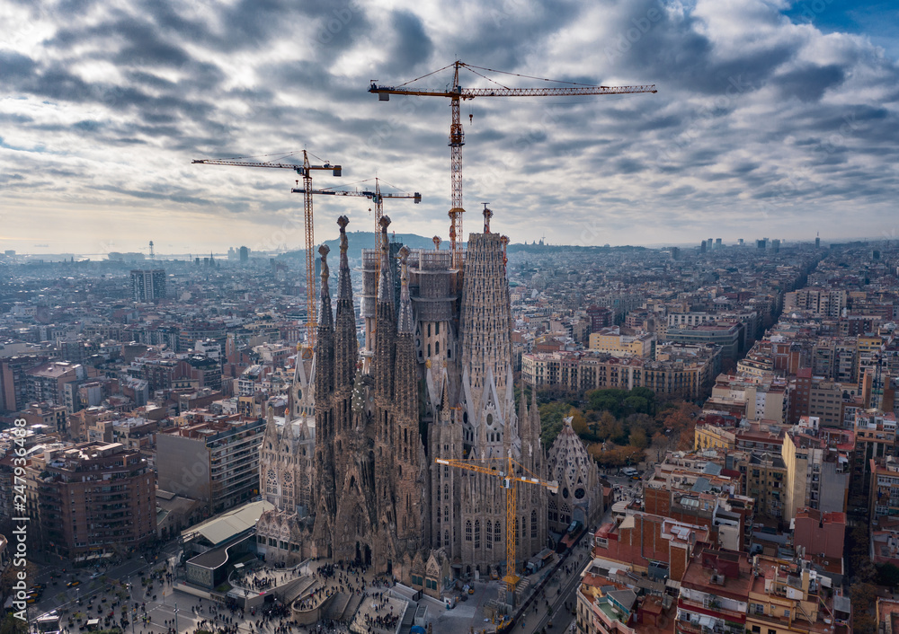 Aerial; drone view of main Gaudi project Sagrada Familia Temple; majestic building towering over the rooftops of Eixample district; long construction of the temple 