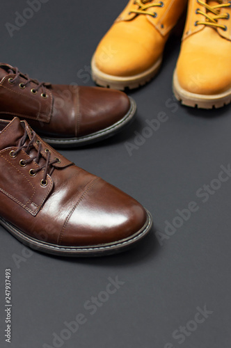 Classic brown leather men's shoes and Yellow men's work boots from natural nubuck on gray black background top view flat lay copy space. Fashion male concept, genuine leather shoes, sale, shop.