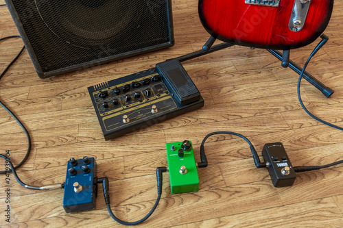 Setting up guitar audio processing effects. Electric guitar stomp box effectors and cables on studio floor next to guitar amp and guitar.