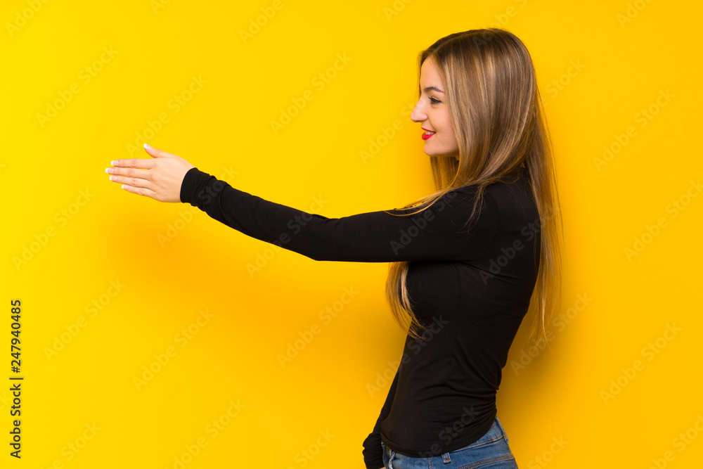 Young pretty woman over yellow background handshaking after good deal Young pretty woman over yellow background handshaking after good deal