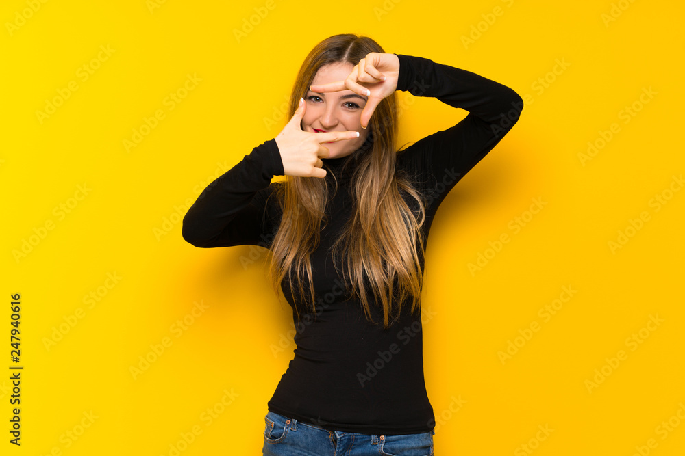 Young pretty woman over yellow background focusing face. Framing symbol Young pretty woman over yellow background focusing face. Framing symbol