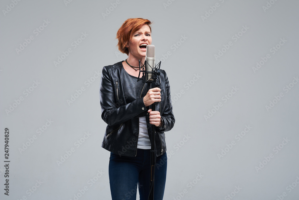 Portrait of rock singer wearing leather jacket and keeping static mic, sings a song loudly on grey background. Concept of rock music and rave Portrait of rock singer wearing leather jacket and keeping static mic, sings a song loudly on grey background. Concept of rock music and rave