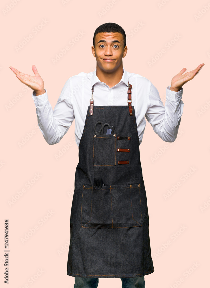 Young afro american barber man having doubts while raising hands and shoulders on isolated background Young afro american barber man having doubts while raising hands and shoulders on isolated background