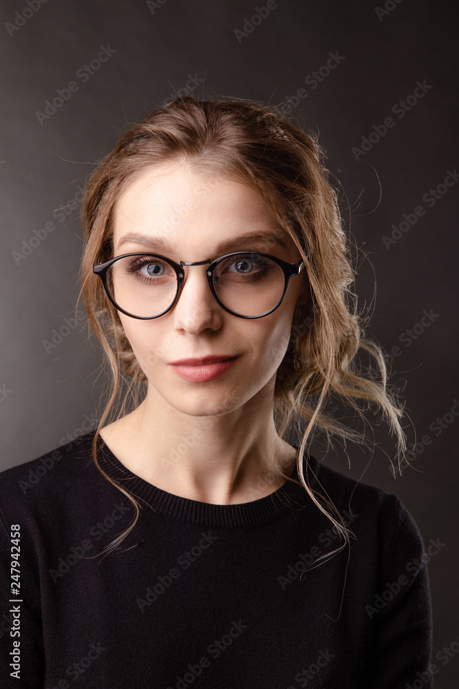 Front view of nice girl in a black clothes and spectacles whatcing camera and posing , portrait of handsome woman in spectacles on the grey backgrownd Front view of nice girl in a black clothes and spectacles whatcing camera and posing , portrait of handsome woman in spectacles on the grey backgrownd
