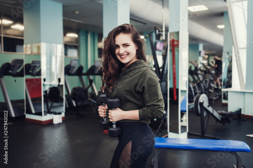 Happy girl in the gym posing with a barbell, in a beautiful sports uniform