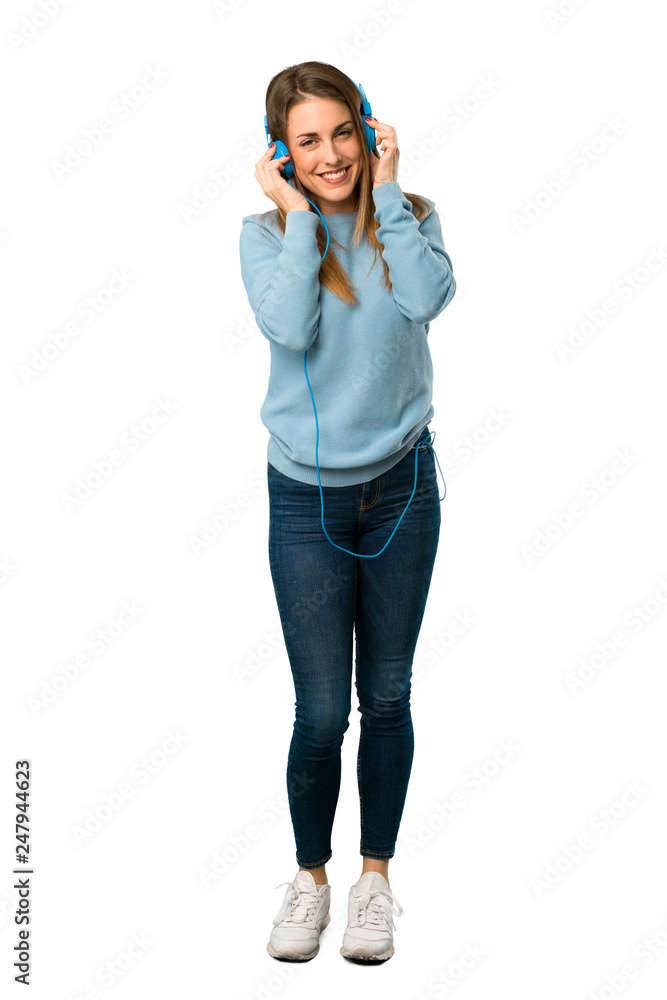 Full body of Blonde woman with blue shirt listening to music with headphones on white background Full body of Blonde woman with blue shirt listening to music with headphones on white background