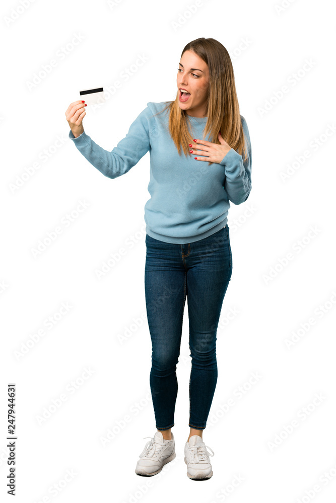Obraz premium Full body of Blonde woman with blue shirt holding a credit card and surprised on white background
