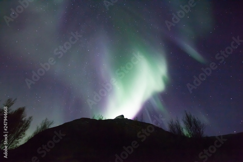 northern lights in Norway in green, blue and violet colours and a silhouette of a mountains in front