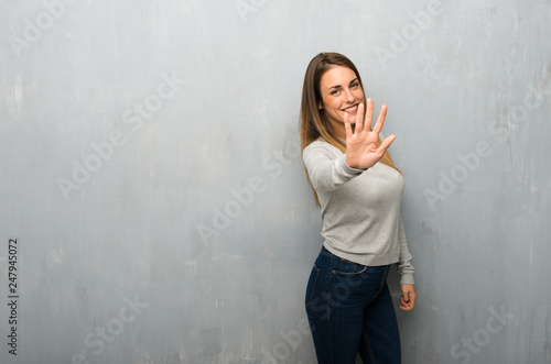 Young woman on textured wall counting five with fingers
