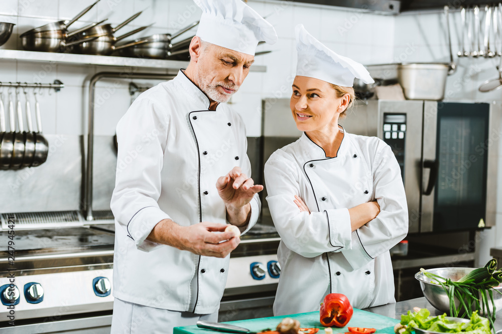 female and male chefs in uniform having conversation while cooking in restaurant kitchen