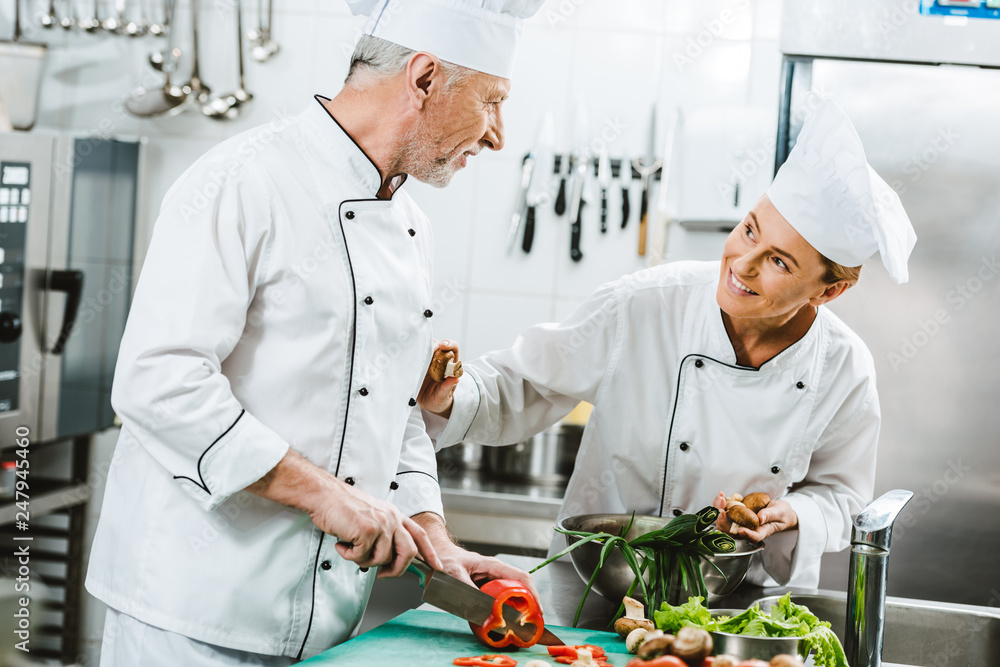 female and male chefs in uniform and hats cooking in restaurant kitchen
