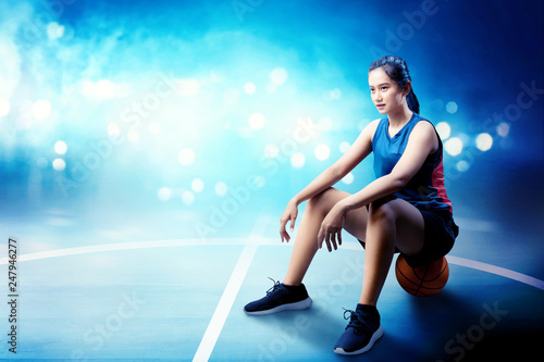 Smiling asian basketball player woman sitting on the ball