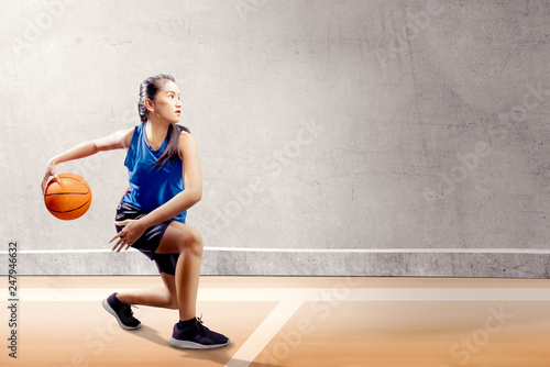 Attractive asian girl in blue sport uniform on basketball pivot moves on the basketball court photo