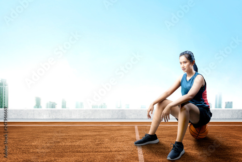 Happy asian woman with sport jersey sitting on the basketball