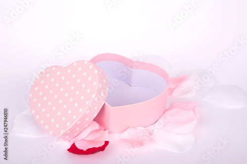 pink gift box with white polka dots and heart shape on white background and petals 