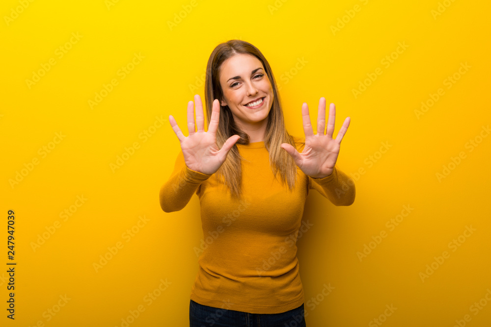 Young woman on yellow background counting ten with fingers Young woman on yellow background counting ten with fingers