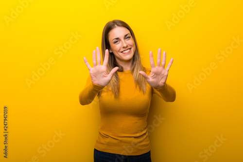 Young woman on yellow background counting ten with fingers