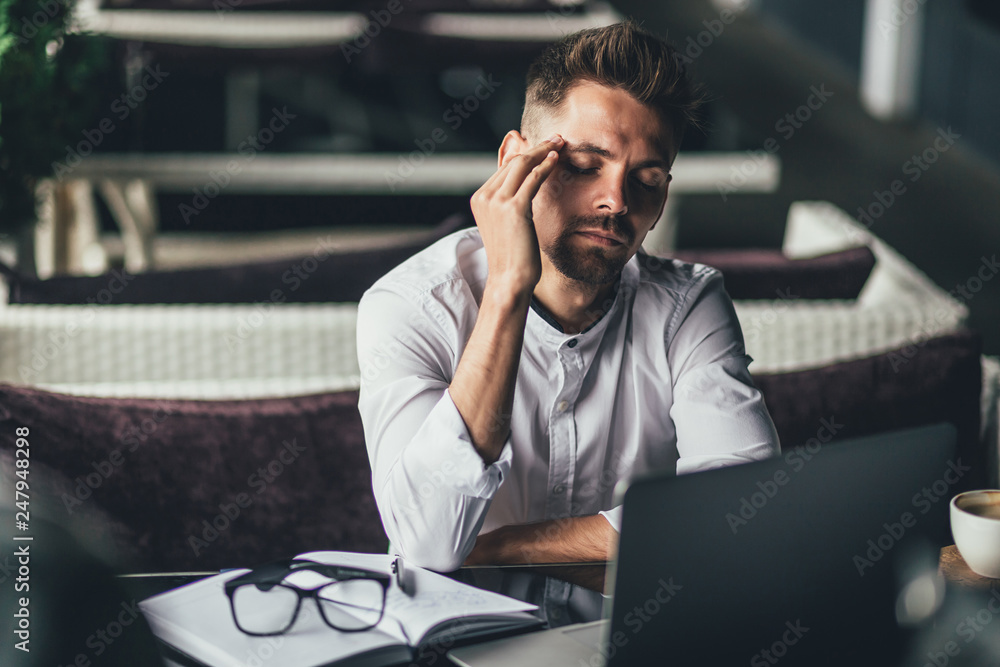 Businessman feeling headache while doing distance work in coffee shop tired with failure of plans, male entrepreneur overworked solving problems with startup project exhausted with hard schedule