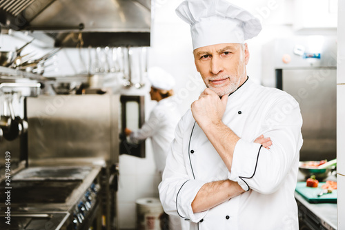 handsome male chef propping chin with hand and looking at camera in restaurant kitchen
