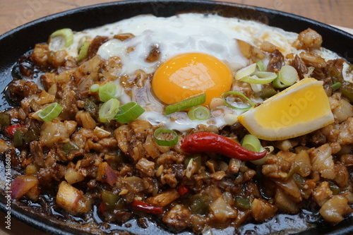 Pork sisig sizzling mince pork Filipino food with raw egg cooking hot on clay pot tray with lemon slice and fresh red chilies Asian cuisine tasty food with pepper on plate  photo