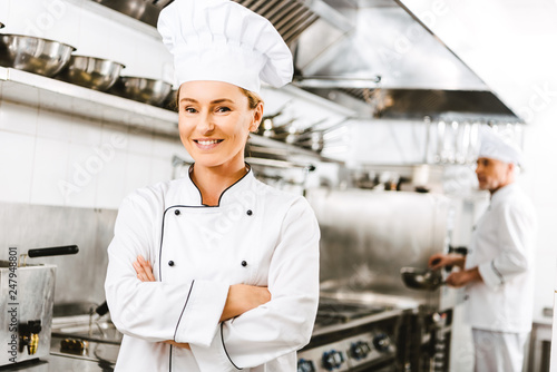 beautiful smiling female chef in uniform with arms crossed looking at camera in restaurant kitchen