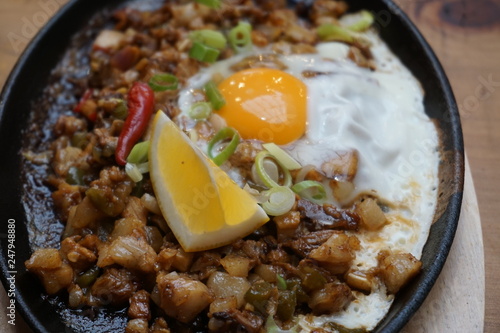 Pork sisig sizzling mince pork Filipino food with raw egg cooking hot on clay pot tray with lemon slice and fresh red chilies Asian cuisine tasty food with pepper on plate 