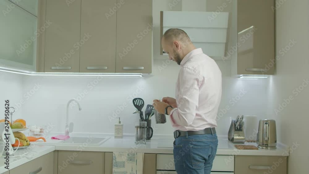 Handsome single man in casual clothes making flavour tea in domestic kitchen during morning breakfast. Positive man adding tea leaves into teapot while preparing lunch at home. Handsome single man in casual clothes making flavour tea in domestic kitchen during morning breakfast. Positive man adding tea leaves into teapot while preparing lunch at home.