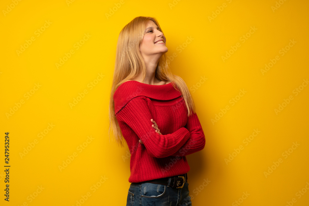 Blonde woman over yellow wall keeping the arms crossed while smiling Blonde woman over yellow wall keeping the arms crossed while smiling