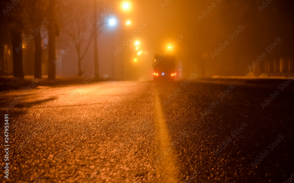 Fog on the streets of the night city. Asphalt road and car in fog. wet asphalt, dangerous slippery road in the winter season. Street lights. car rear lights. selective focus