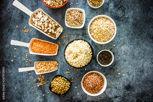 Cereals and legumes in the range. Peas, beans, lentils, rice, quinoa, chia seeds, oatmeal, in small cups and scoops on a dark stone background, culinary background, background about products