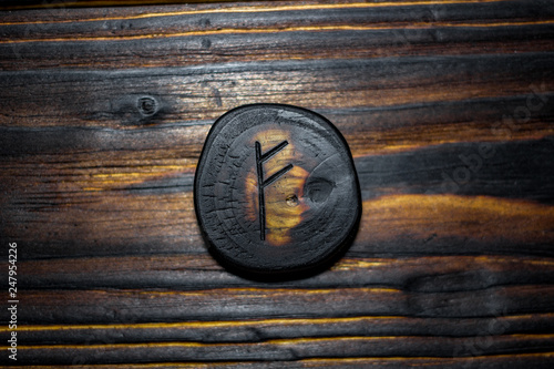 Rune Fehu carved from wood on a wooden background - Elder Futhark photo
