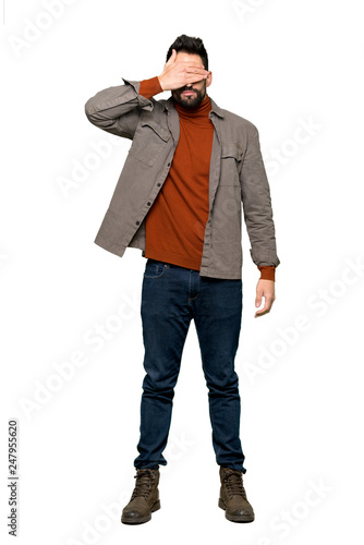 Full-length shot of Handsome man with beard covering eyes by hands. Do not want to see something on isolated white background