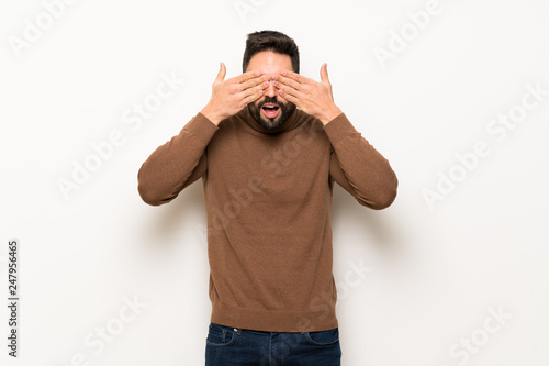 Handsome man over white wall covering eyes by hands. Surprised to see what is ahead