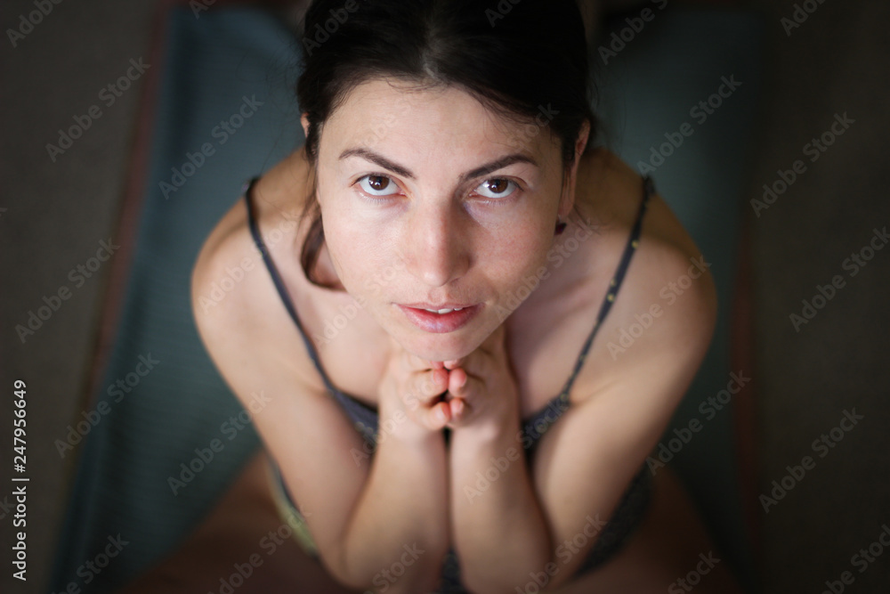 Gorgeous young Europian female on dark background, holding hands in namaste or prayer, keeping eyes open, while practising yoga and meditating at home alone, having calm look on her face Gorgeous young Europian female on dark background, holding hands in namaste or prayer, keeping eyes open, while practising yoga and meditating at home alone, having calm look on her face