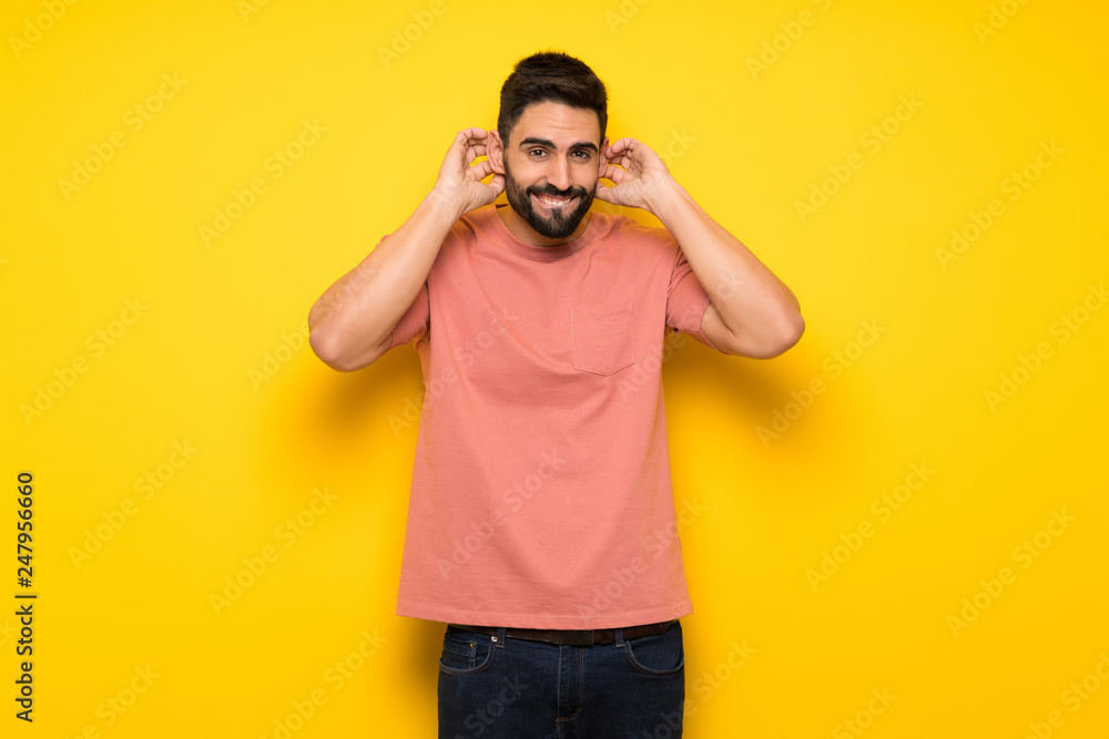 Handsome man over yellow wall covering ears with hands. Frustrated expression Handsome man over yellow wall covering ears with hands. Frustrated expression