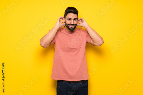 Handsome man over yellow wall covering ears with hands. Frustrated expression