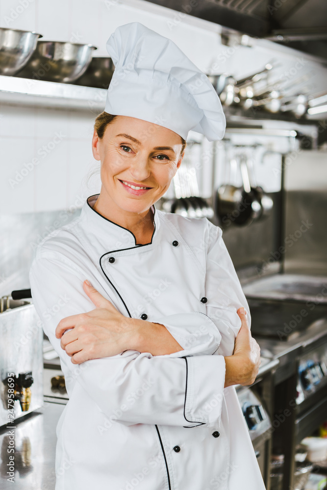 attractive female chef in uniform with arms crossed looking at camera in restaurant kitchen