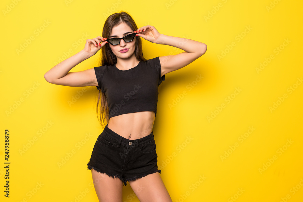 Carefree summer. Beautiful girl in summer clothes and sunglasses standing on yellow background.