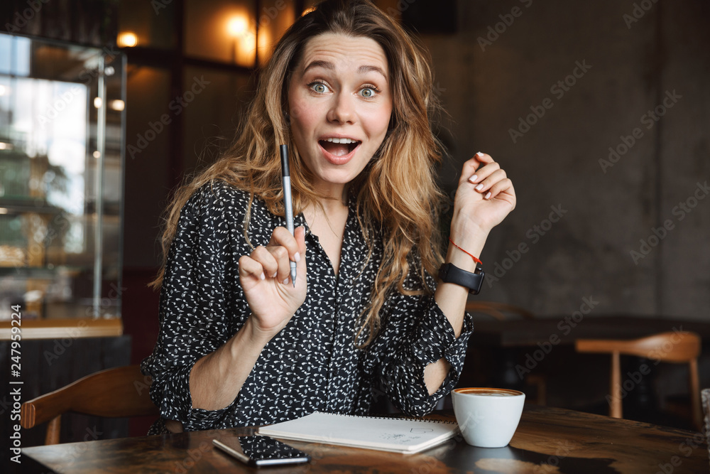 Beautiful young pretty woman sitting in cafe indoors writing notes in notebook drinking coffee. Beautiful young pretty woman sitting in cafe indoors writing notes in notebook drinking coffee.