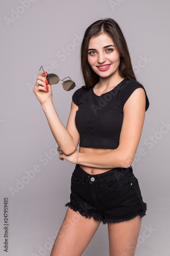 Pretty young woman holding sunglasses isolated light grey gray background