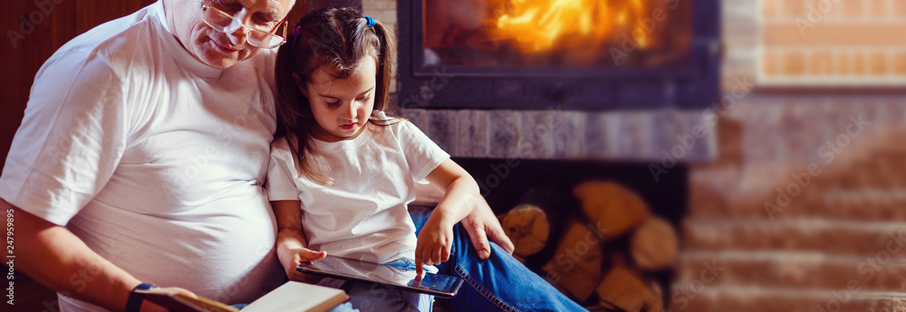 Obraz premium Little girl and her grandfather sitting on sofa in living room decorated for Christmas