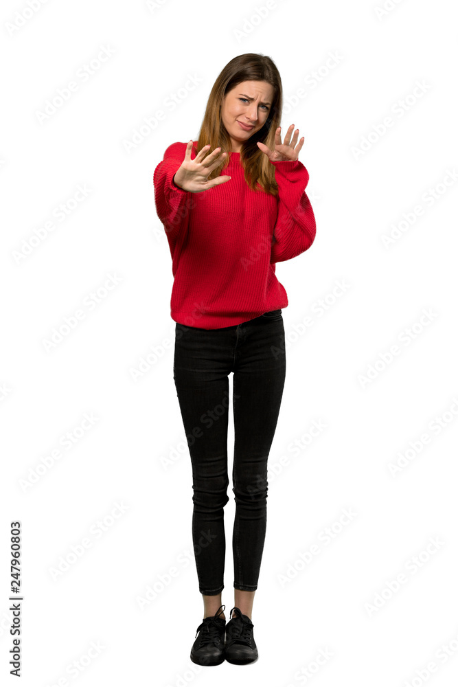 Fototapeta premium A full-length shot of a Young woman with red sweater nervous and scared stretching hands to the front over isolated white background