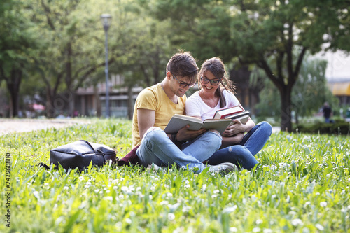 Two young students sitting at the campus yard, reading a book and preparing for a university exam. © BalanceFormCreative
