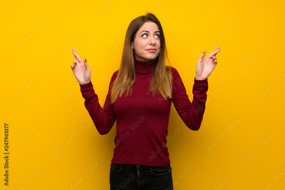 Woman with turtleneck over yellow wall with fingers crossing and wishing the best Woman with turtleneck over yellow wall with fingers crossing and wishing the best