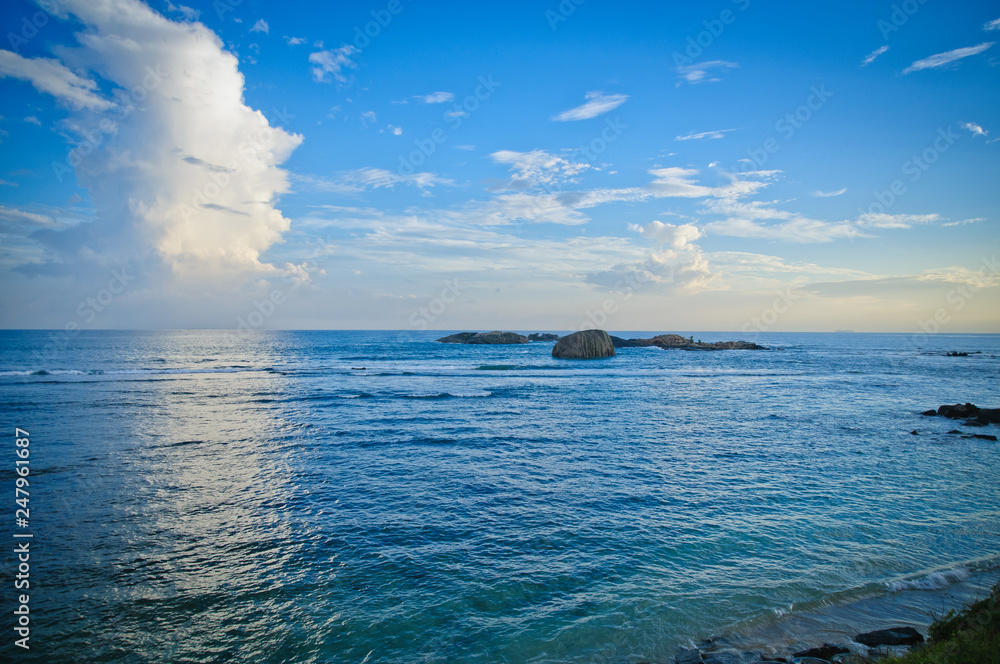 Fototapeta premium Ocean and blue sky with clouds. Rocks in the water.