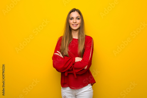 Young girl with red dress over yellow wall keeping the arms crossed in frontal position