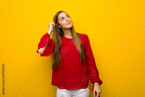 Young girl with red dress over yellow wall thinking an idea while scratching head